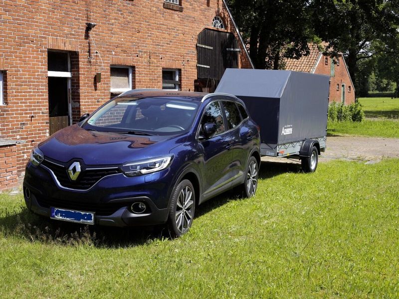 Auto mit angekuppeltem Planenanhänger vor einem Bauernhaus
