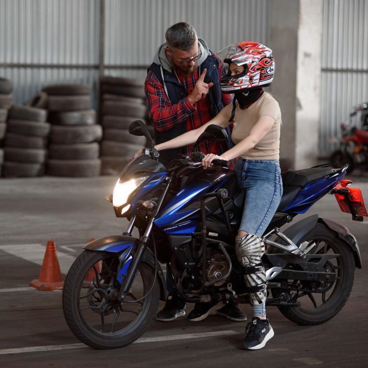 Fahrlehrer erklärt einer Fahrschülerin auf dem Motorrad eine Übung