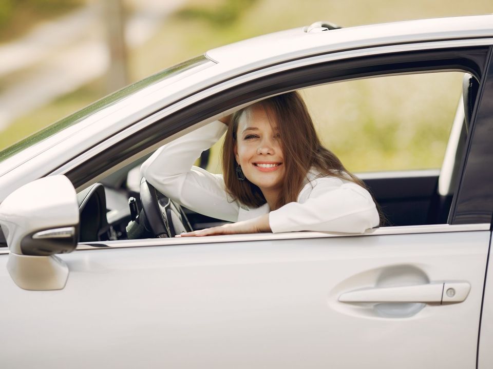 Lächelnde junge Frau am Steuer eines weißen Autos