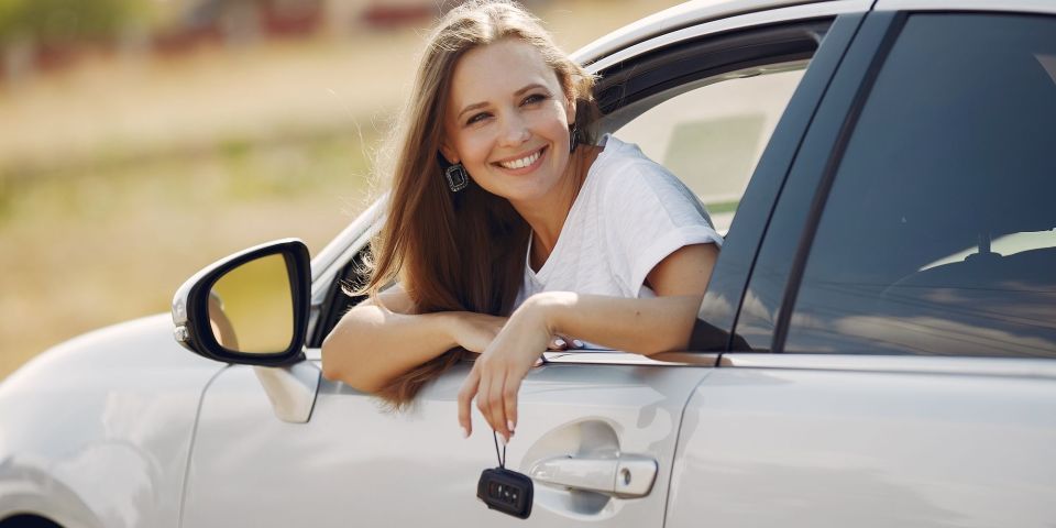 Junge Frau hält lachend einen Autoschlüssel aus dem Autofenster